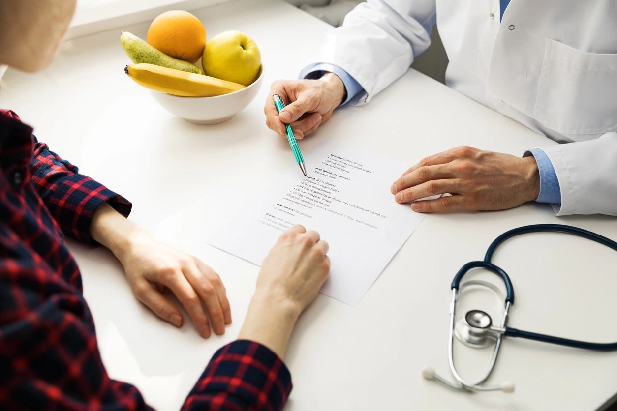 Over-the-shoulder view of a doctor or nutritionist reviewing a healthy meal plan sheet with a patient.