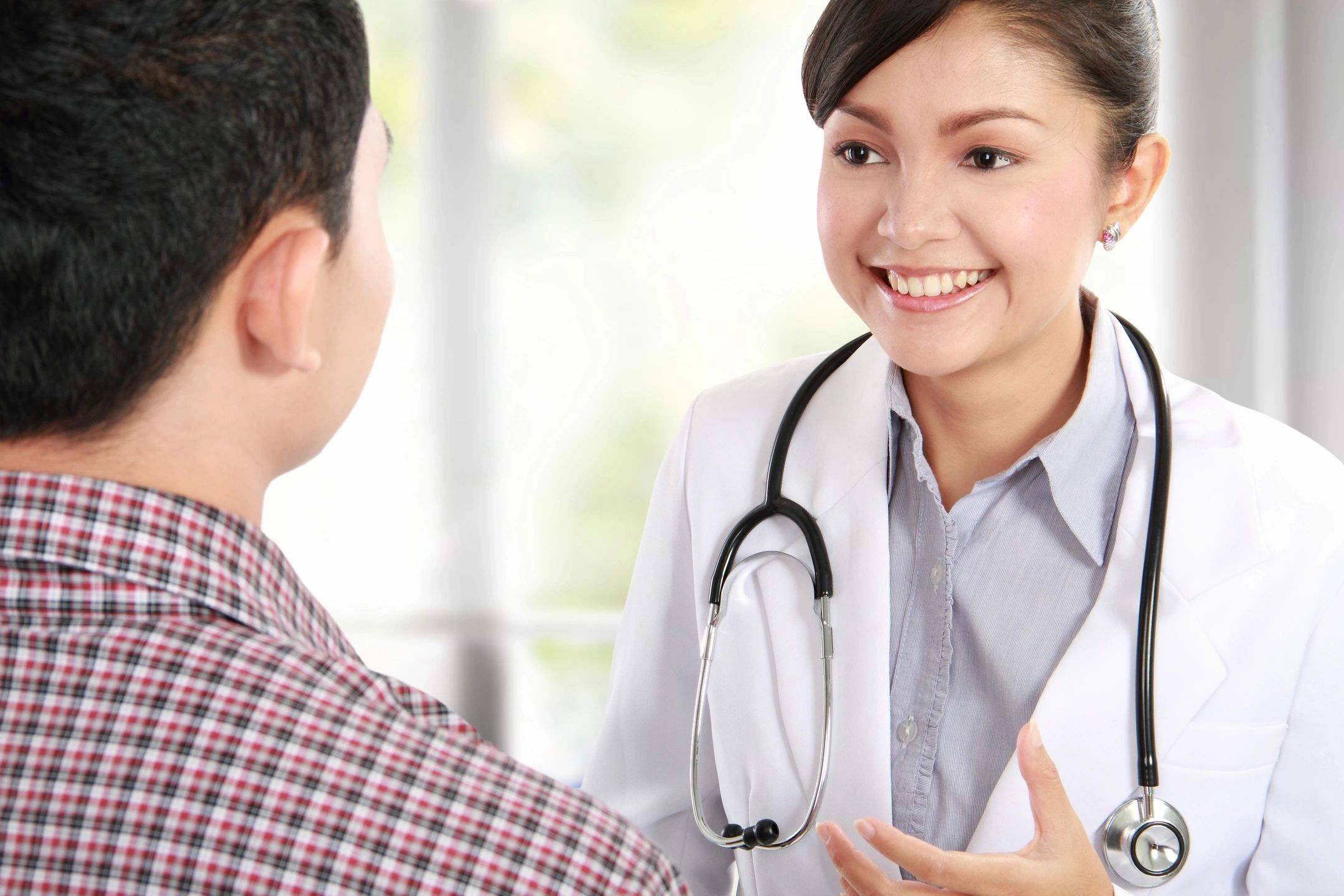 A smiling female healthcare professional with a stethoscope talking reassuringly to a male patient.