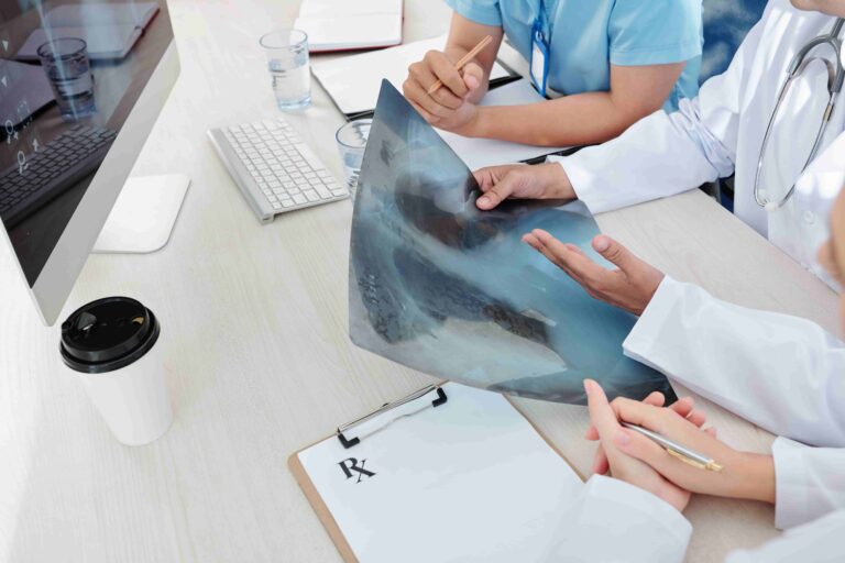 A pulmonologist holding and discussing a chest X-ray scan during a medical team consultation at a desk.