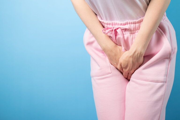 A woman holding her lower abdomen in discomfort due to urinary incontinence against a blue background.